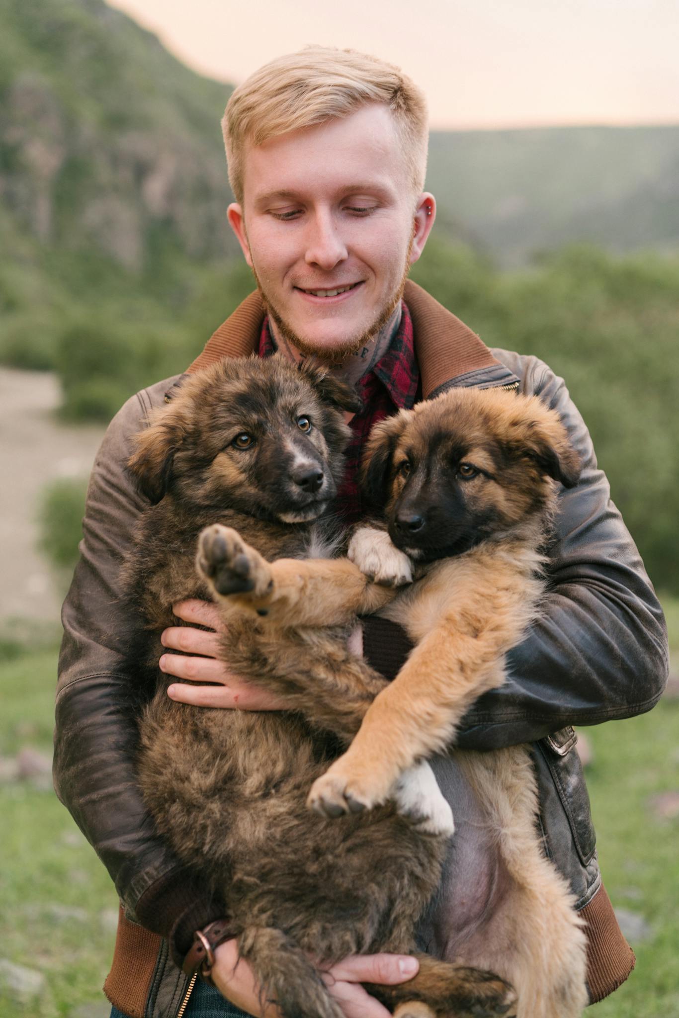 A happy man holding two adorable puppies in a scenic outdoor setting.